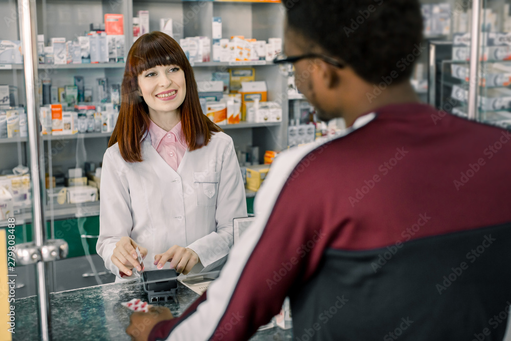 Obraz premium African man customer making payment in drugstore. Pharmacist woman holding terminal, man paying for medicaments with credit card.