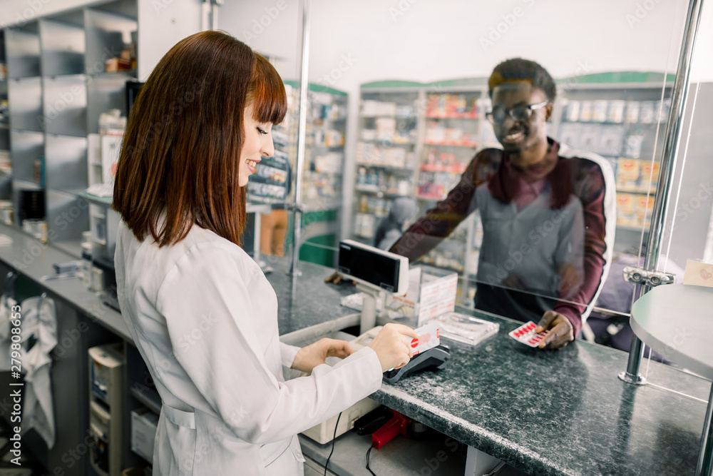 Young African man paying for pills with credit card in pharmacy. Smiling woman pharmacist giving pills to black man in drugstore Young African man paying for pills with credit card in pharmacy. Smiling woman pharmacist giving pills to black man in drugstore