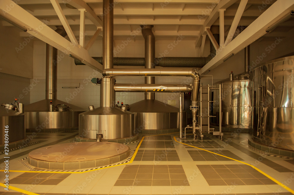 Fototapeta premium Equipment for preparation of beeer..Lines of metal tanks in modern brewery. Manufacturable process of brewage. Mode of beer production. Inside view of modern brewhouse with stainless barrels
