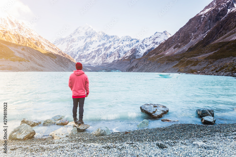 Tourist in red jacket standing in front of Hooker Lake enjoying the landscape of Aoraki Mount Cook, New Zealand 