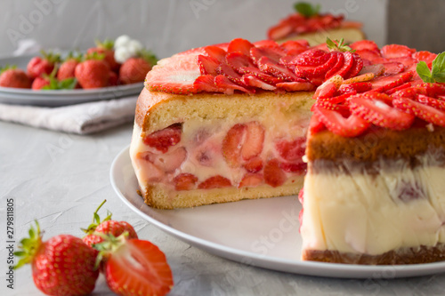 Cut biscuit cake with strawberries and vanilla jelly decorated with strawberry slices and mint leaves on a gray background. Fraisier cake .Horizontal orientation, side view.