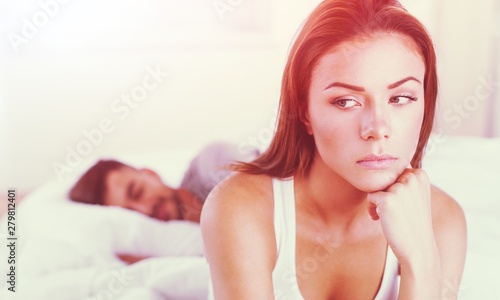 Photography Dissatisfied beautiful young woman in bed with sad expression on her face, sex problems in long relationship or marriage while man sleeping