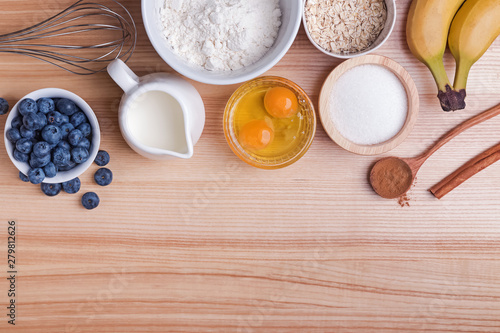 Ingredients for blueberry muffins preparation on wooden table, top view.