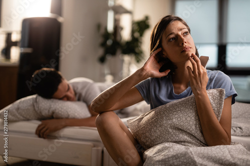 Pensive woman with mobile phone thinking of something while her boyfriend is sleeping.