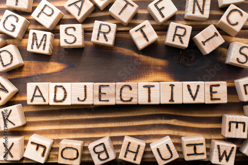 word adjective composed of wooden cubes with letters, Part of speech concept scattered around the cubes random letters, top view on wooden background