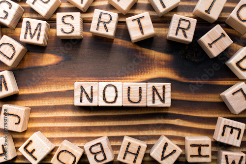 word noun composed of wooden cubes with letters, Part of speech concept scattered around the cubes random letters, top view on wooden background photo