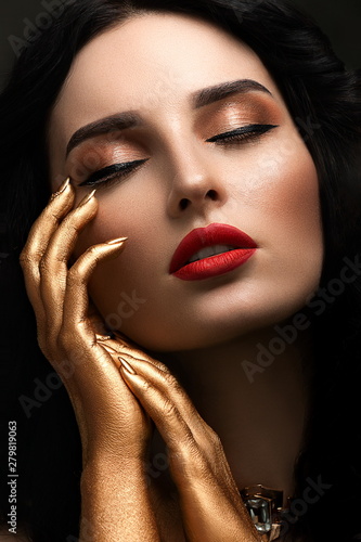 Close-up portrait of beautiful young woman with bright red lipstick and golden hands