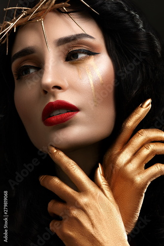 Close-up portrait of beautiful young woman with bright red lipstick and golden hands and tears