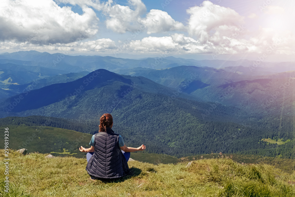Woman in meditation pose sitting on the top of the mountain