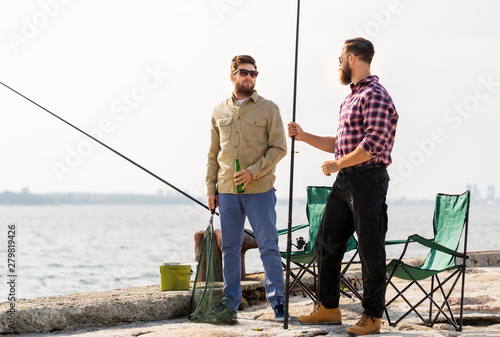 leisure and people concept - male friends with fishing rods and beer on pier at sea