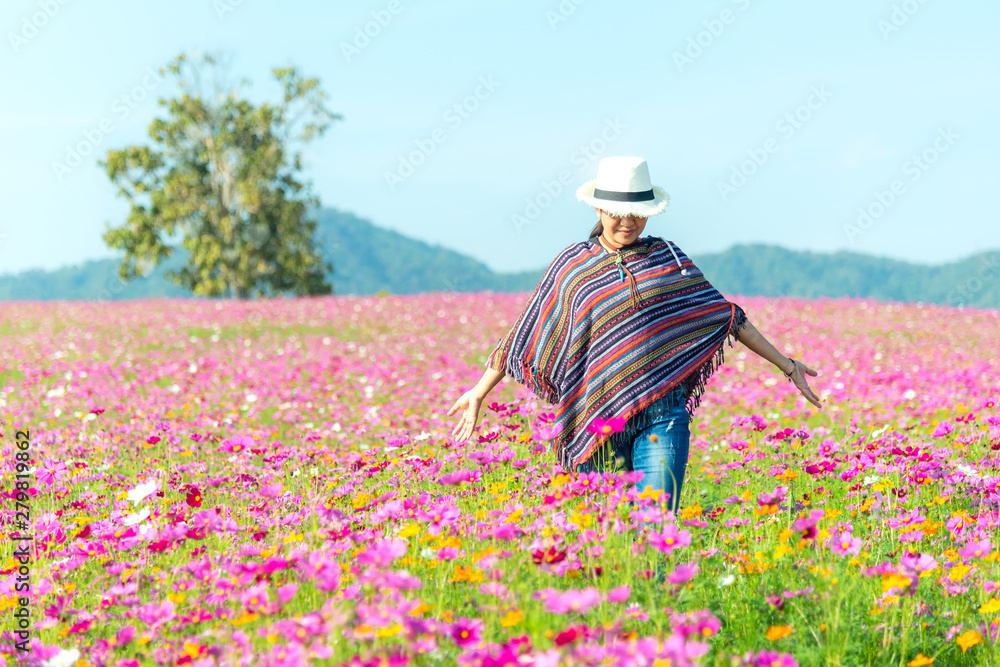 Traveler Asian women walking in the flower field and hand touch cosmos flower, freedom and relax in the flower meadow, blue sky background. Lifestyle Concept