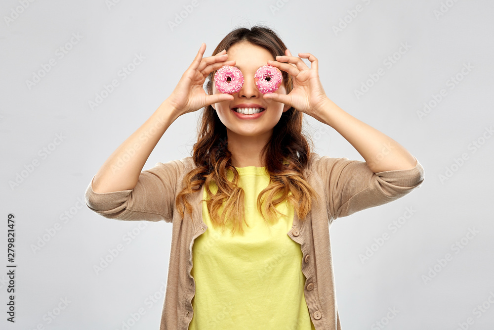 people, fast food and fun concept - happy asian young woman with donuts instead of eyes over grey background people, fast food and fun concept - happy asian young woman with donuts instead of eyes over grey background