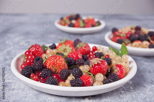 Healthy mixed berry with strawberry  blackberry  red and white currant on the different plates on concrete background. Top view. Copy space.