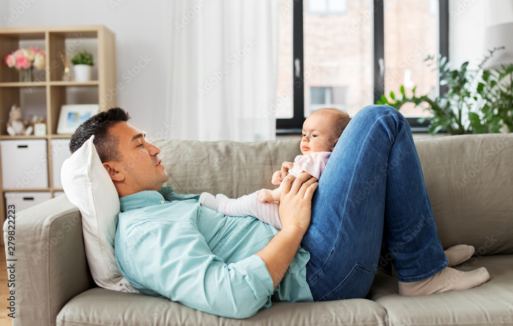 family, parenthood and fatherhood concept - happy middle aged father with little baby daughter lying on sofa at home - obrazy, fototapety, plakaty 