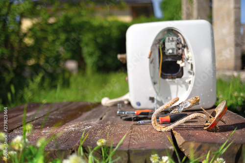 Heating element, rust and scale on boiler background, lying on wooden table. Yard on the background. Copy space photo