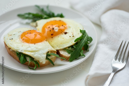 Sandwiches with ricotta cheese, arugula and fried egg on white wooden background. Selective focus. Healthy food concept