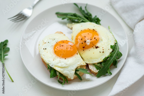 Sandwiches with ricotta cheese, arugula and fried egg on white wooden background. Selective focus. Healthy food concept