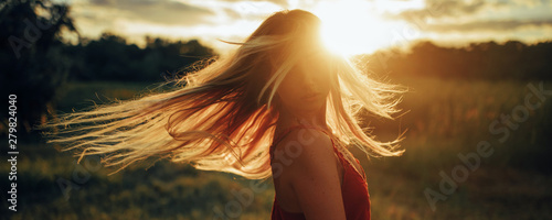 Slika na platnu Young blond woman stands on meadow with loose hair lit by sun.