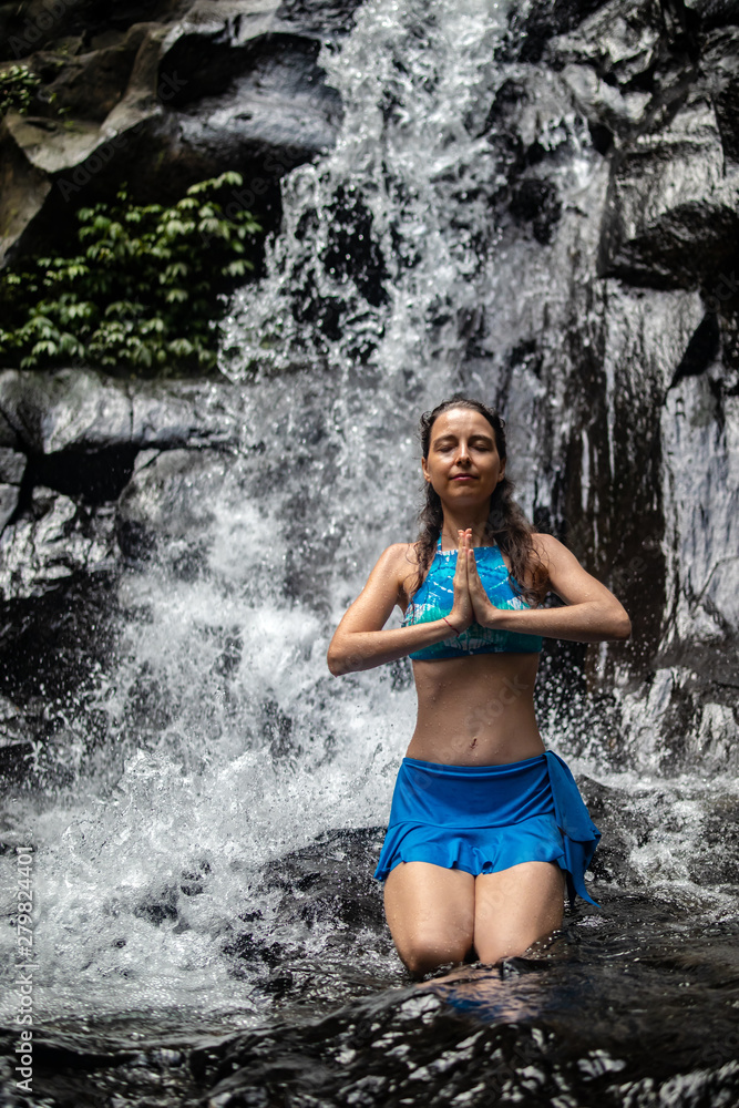 Young Caucasian woman meditating, practicing yoga at waterfall in Ubud, Bali, Indonesia. Close up. Young Caucasian woman meditating, practicing yoga at waterfall in Ubud, Bali, Indonesia. Close up.