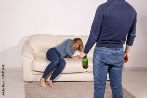 People, violence and abuse concept - Man drinking alcohol while wife is lying on sofa