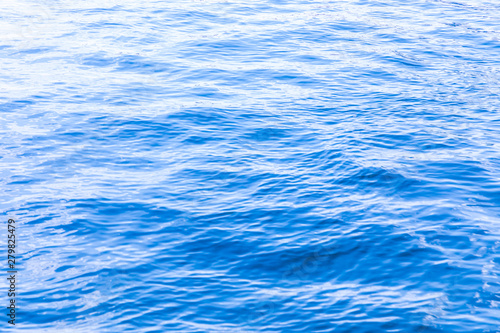 The background or texture of the blue water surface of the river, lake or sea with the waves, ripples and flares
