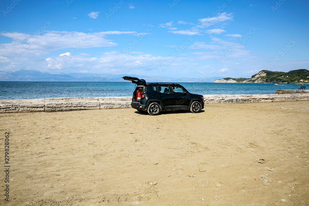 Black summer car on the sunny sandy beach. Blue clear sunshine sky view in distance. Black summer car on the sunny sandy beach. Blue clear sunshine sky view in distance.