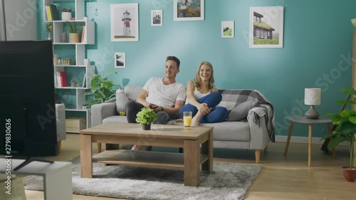 Happy young couple watching tv on couch in cozy living room