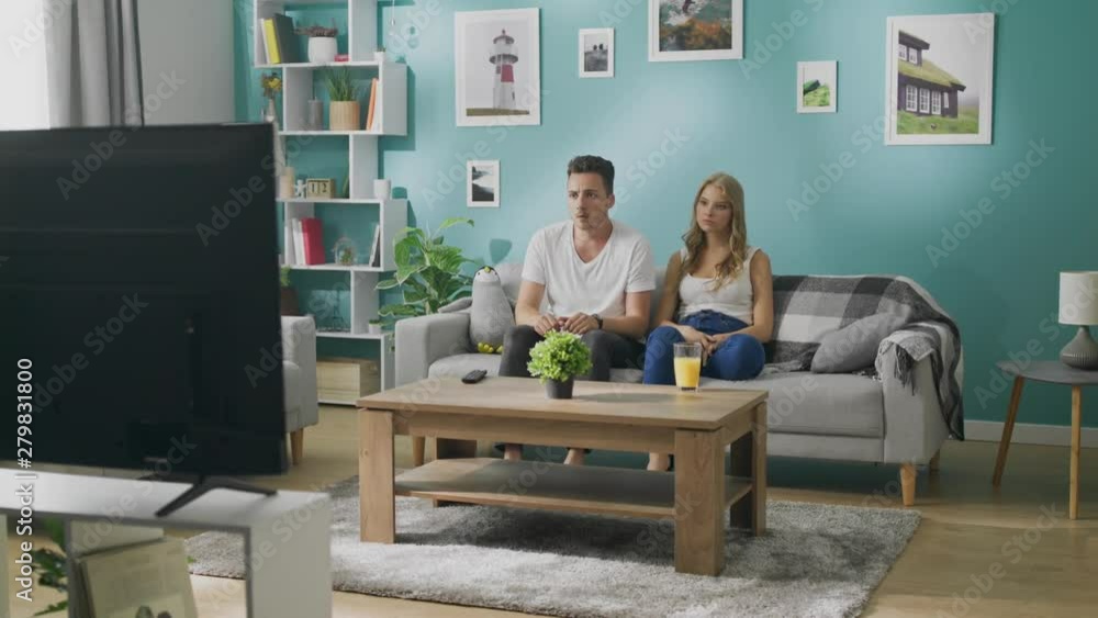 Young couple watching a scary movie on TV on the couch in a cozy living room Young couple watching a scary movie on TV on the couch in a cozy living room