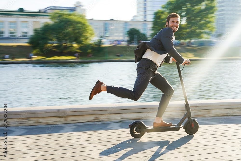 Young business man in a suit riding an electric scooter on a business  meeting. Photos | Adobe Stock