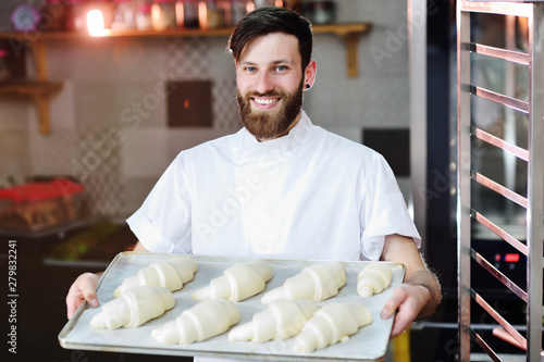 Baker puts in the oven raw croissants on the background of the bakery photo