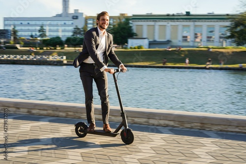 Young business man in a suit riding an electric scooter on a business meeting.