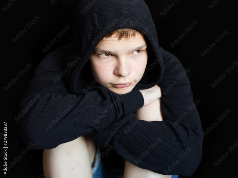 portrait of a sad, lonely, brooding teenager in a black sweatshirt on a dark background. The concept of teenage problems portrait of a sad, lonely, brooding teenager in a black sweatshirt on a dark background. The concept of teenage problems