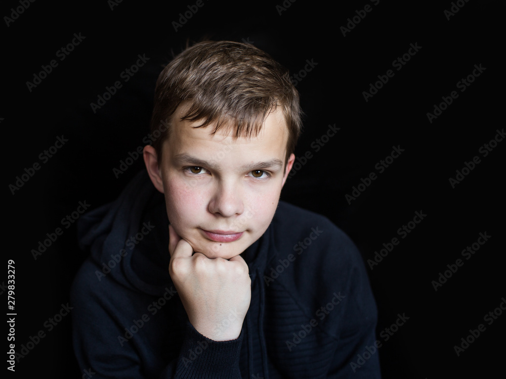 portrait of a sad, lonely, brooding teenager in a black sweatshirt on a dark background. The concept of teenage problems portrait of a sad, lonely, brooding teenager in a black sweatshirt on a dark background. The concept of teenage problems