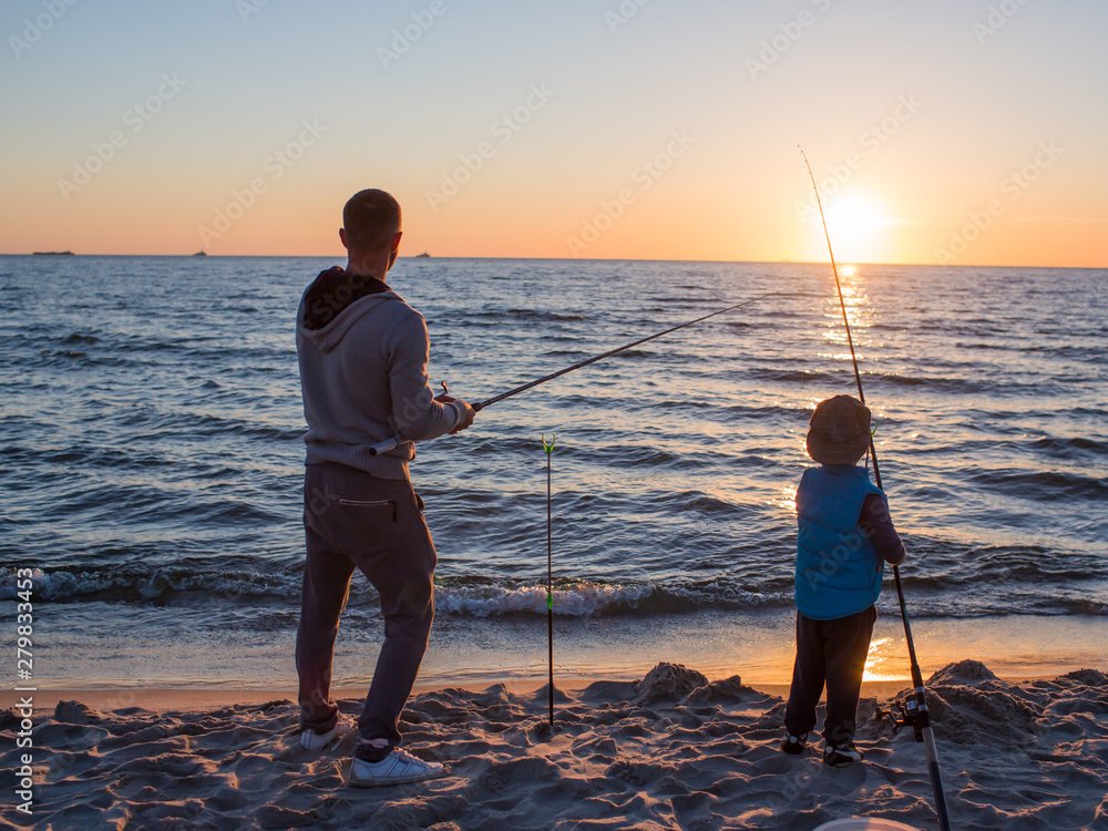 Father and son fishing on the beach of Baltic Sea in the sunset time.