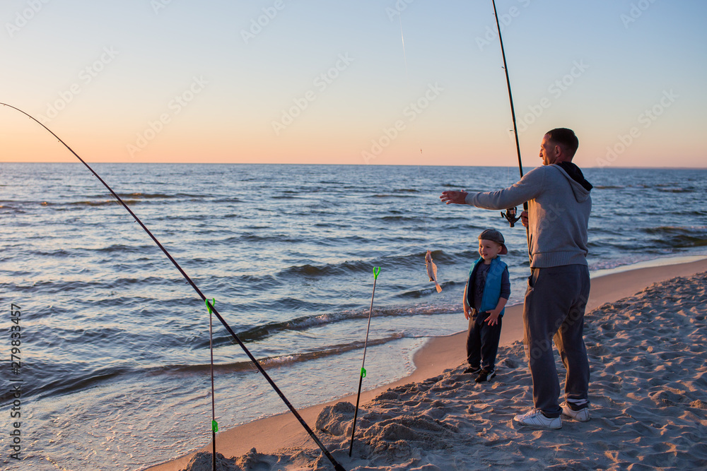 Father and son fishing on the beach of Baltic Sea in the sunset time.