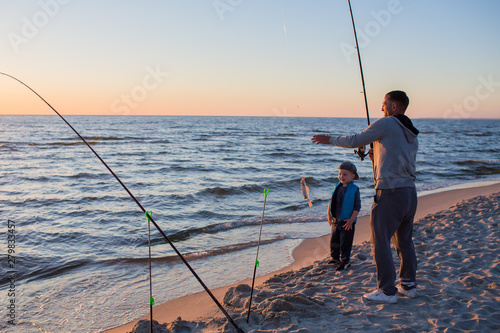 Obraz na płótnie Father and son fishing on the beach of Baltic Sea in the sunset time. w salonie