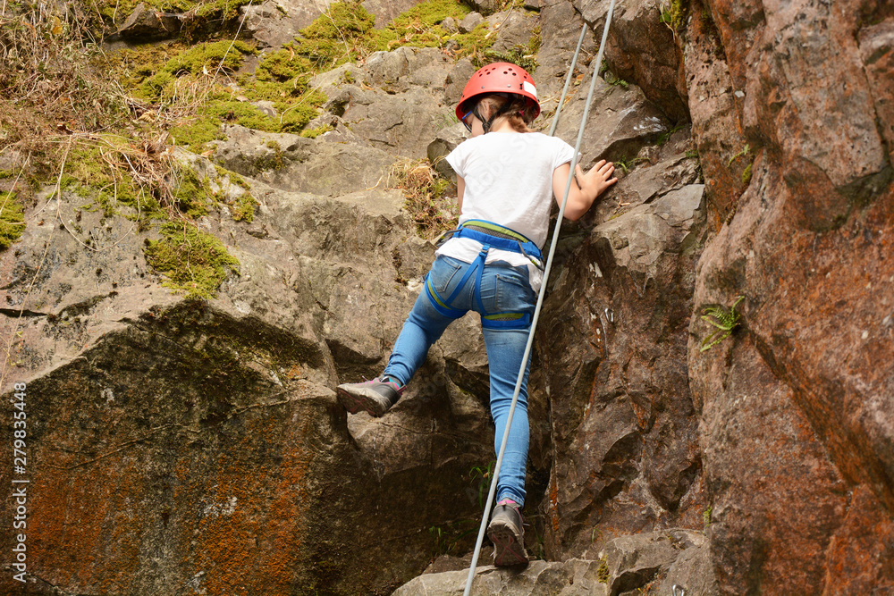 Fototapeta premium Little girl with protective equipment climbs up rock or mountain
