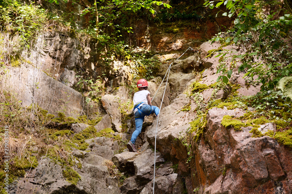 Little girl with protective equipment climbs up rock or mountain