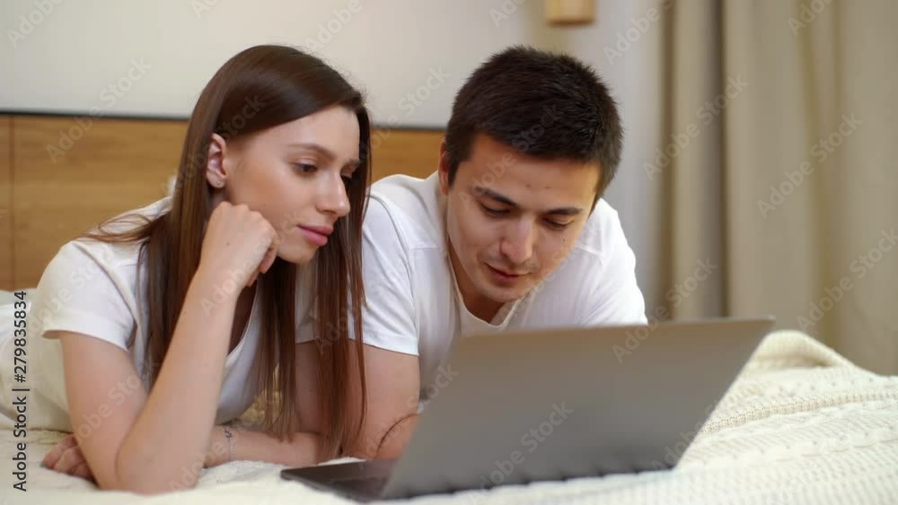 Close-up portrait of young handsome couple lying on bed in the evening and watching something funny on the laptop computer. Close-up portrait of young handsome couple lying on bed in the evening and watching something funny on the laptop computer.