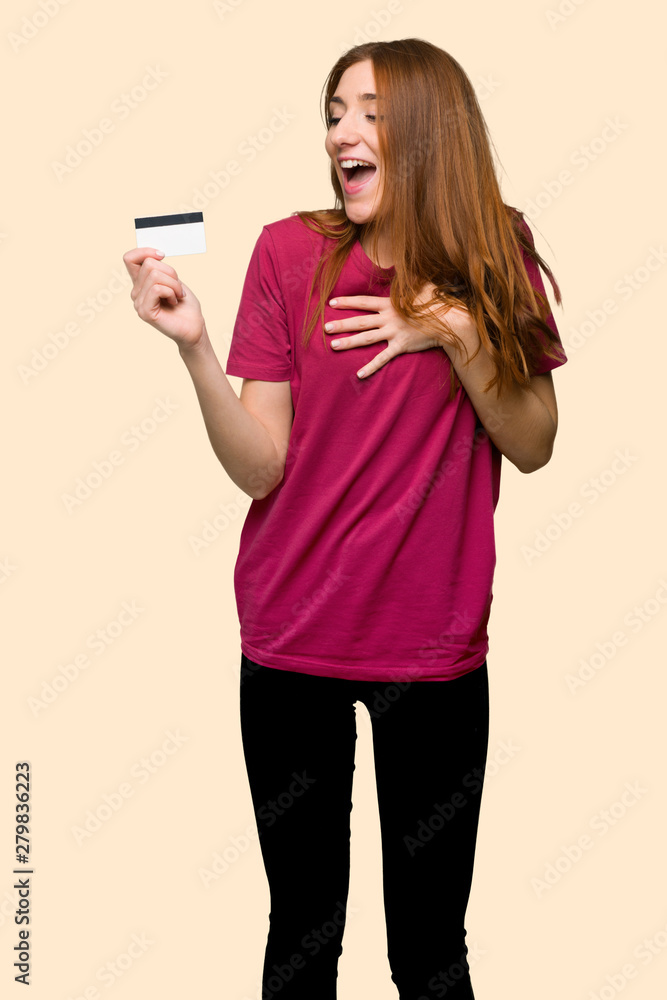 Young redhead girl holding a credit card and surprised on isolated yellow background Young redhead girl holding a credit card and surprised on isolated yellow background