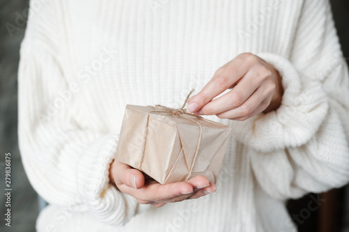 Woman in white knitted sweater giving wrapped gift. Close up Female hands holding Christmas box present. Christmas, New Year, shopping, preparation on Winter Holidays, donation concept. 