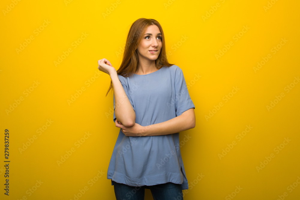 Young redhead girl over yellow wall background with confuse face expression while bites lip Young redhead girl over yellow wall background with confuse face expression while bites lip