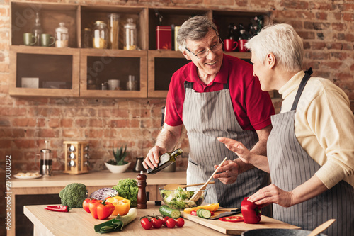Senior man and woman laughing and preparing healthy food at kitchen