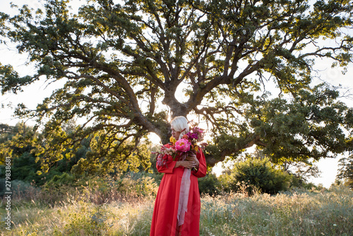 Beautiful young woman with flowers in the field and a tree as a background