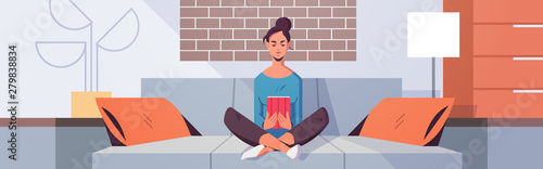 young woman sitting on couch using tablet girl reading e-book e-learning concept modern living room interior flat horizontal full length