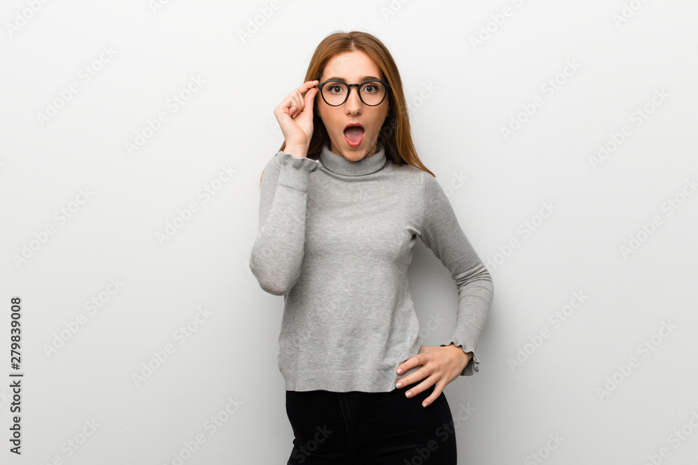 Redhead girl over white wall with glasses and surprised Redhead girl over white wall with glasses and surprised