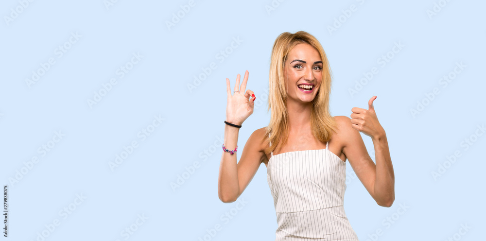 Young blonde woman showing ok sign and thumb up gesture over isolated blue background Young blonde woman showing ok sign and thumb up gesture over isolated blue background