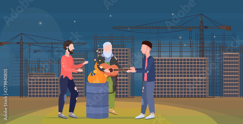 poor men group warming by fire beggars playing guitar standing near burning garbage in barrel homeless jobless unemployment concept construction site background horizontal flat full length