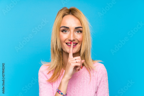 Young blonde woman over blue background doing silence gesture