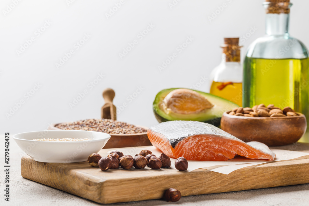 fresh salmon, nuts and avocado on wooden chopping board near oil isolated on grey, ketogenic diet menu fresh salmon, nuts and avocado on wooden chopping board near oil isolated on grey, ketogenic diet menu